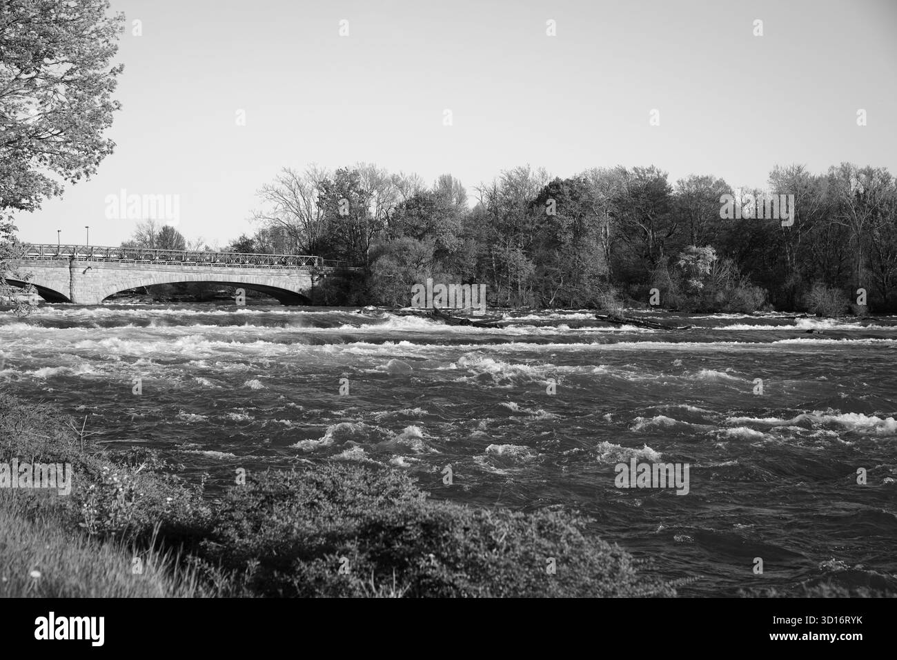 Image en noir et blanc d'un pont piétonnier en pierre traversant la rivière Niagara, encadré par des rapides ondulés et un feuillage printanier luxuriant le long de la rivière Banque D'Images