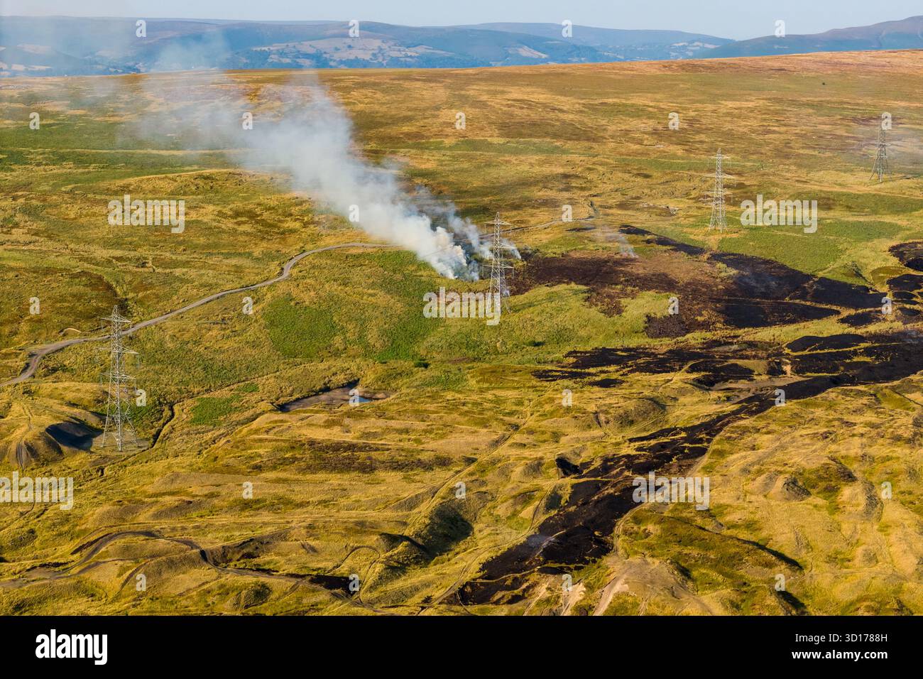 Vue aérienne par drone d'un feu d'herbe et de landes fumant près de pylônes électriques au pays de Galles Banque D'Images