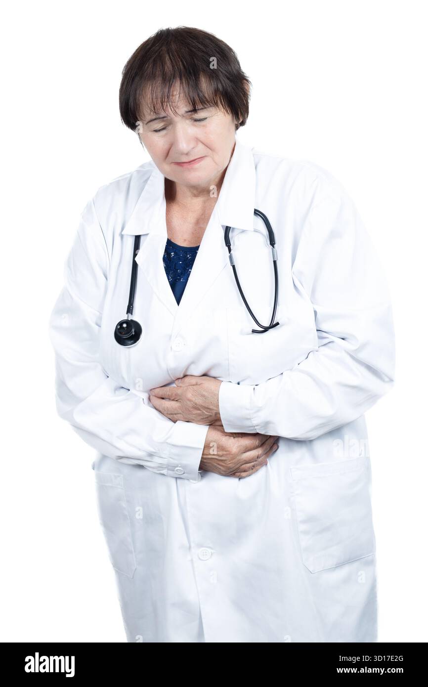 Médecin de femme senior en manteau blanc tient les mains sur son abdomen, griffant dans la douleur de maux d'estomac ou d'inconfort gastro-intestinal pendant la clinique Banque D'Images