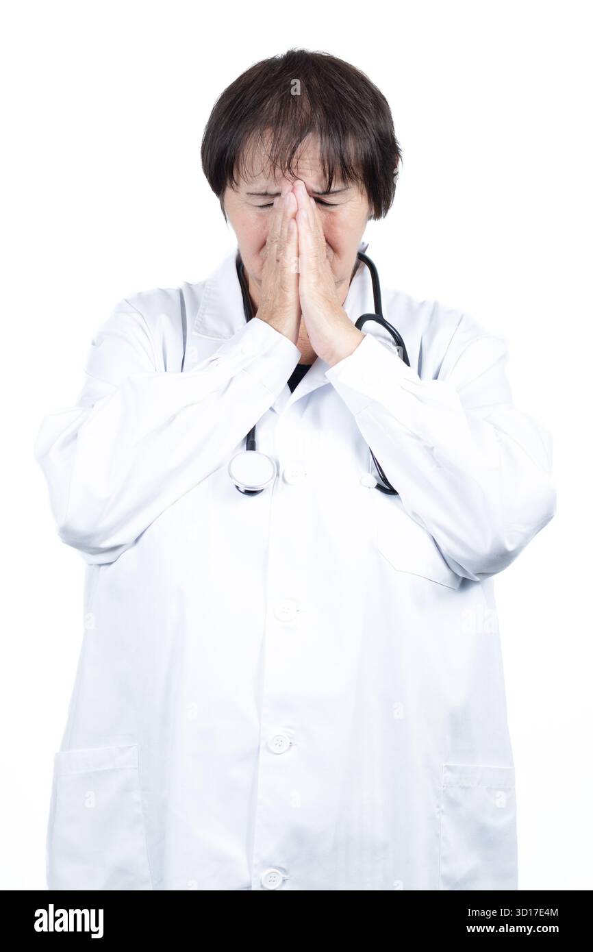 Médecin femme portant une blouse de laboratoire blanche et un stéthoscope éprouvant le stress et l'épuisement professionnel, couvrant son visage avec des mains serrées dans un moment de désespoir Banque D'Images