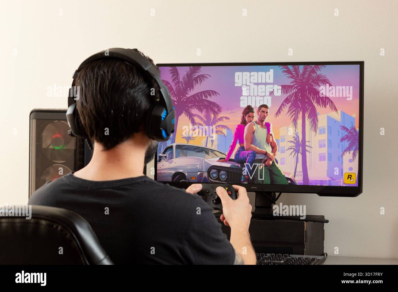 Un jeune joueur masculin tenant une manette xbox et utilisant des écouteurs de joueur regardant un écran avec grand jeu vidéo Theft auto 6 Banque D'Images