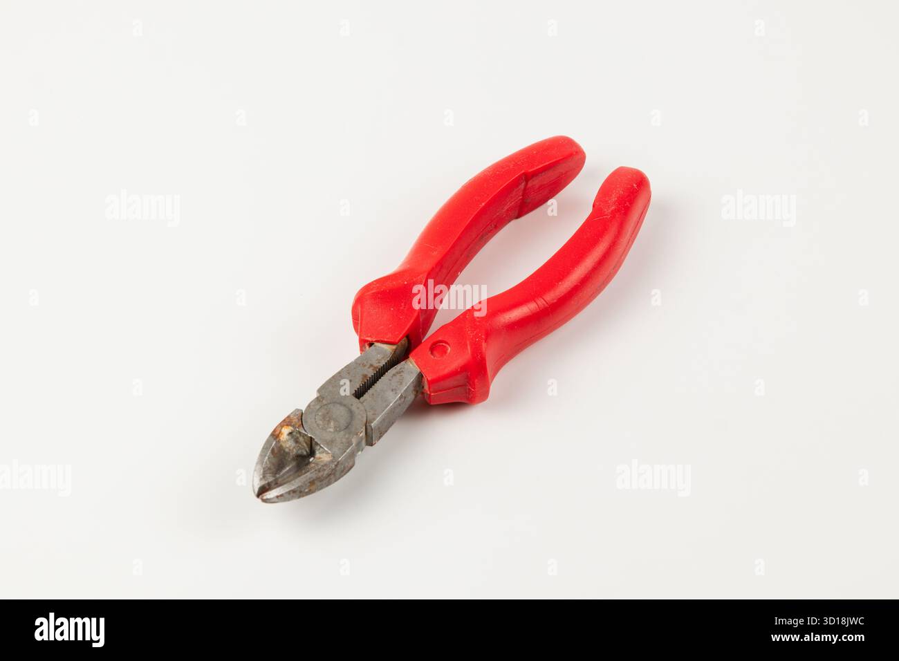 Un outil de coupe de fil avec poignées rouges repose sur une surface blanche lisse. Les arêtes de coupe montrent l'usure, indiquant une utilisation régulière dans divers projets ou repai Banque D'Images