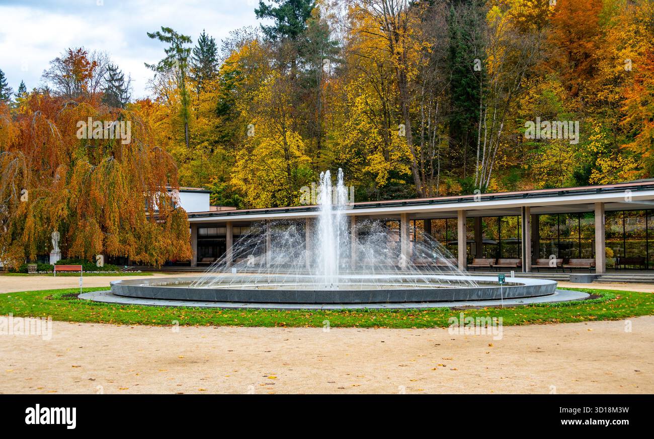Vue d'automne de la place du spa à Luhacovice, République tchèque, avec une fontaine au centre et des arbres colorés en arrière-plan brillants en rouge, orange Banque D'Images