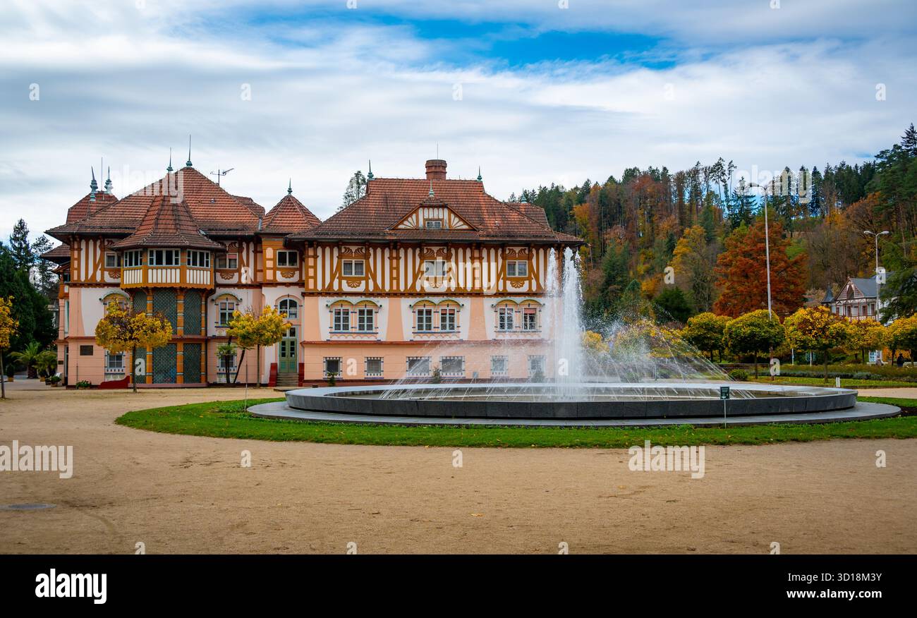Vue d'automne de la place du spa à Luhacovice, République tchèque, avec une fontaine au centre et des arbres colorés en arrière-plan brillants en rouge, orange Banque D'Images