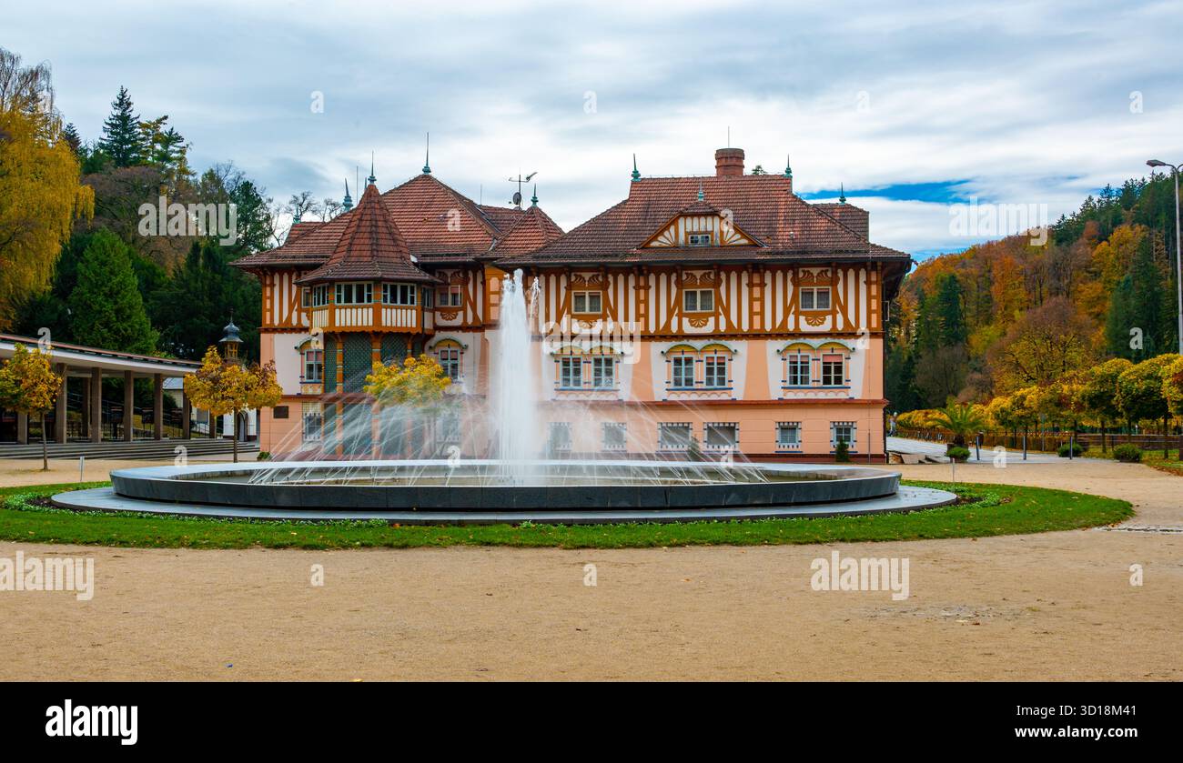 Vue d'automne de la place du spa à Luhacovice, République tchèque, avec une fontaine au centre et des arbres colorés en arrière-plan brillants en rouge, orange Banque D'Images