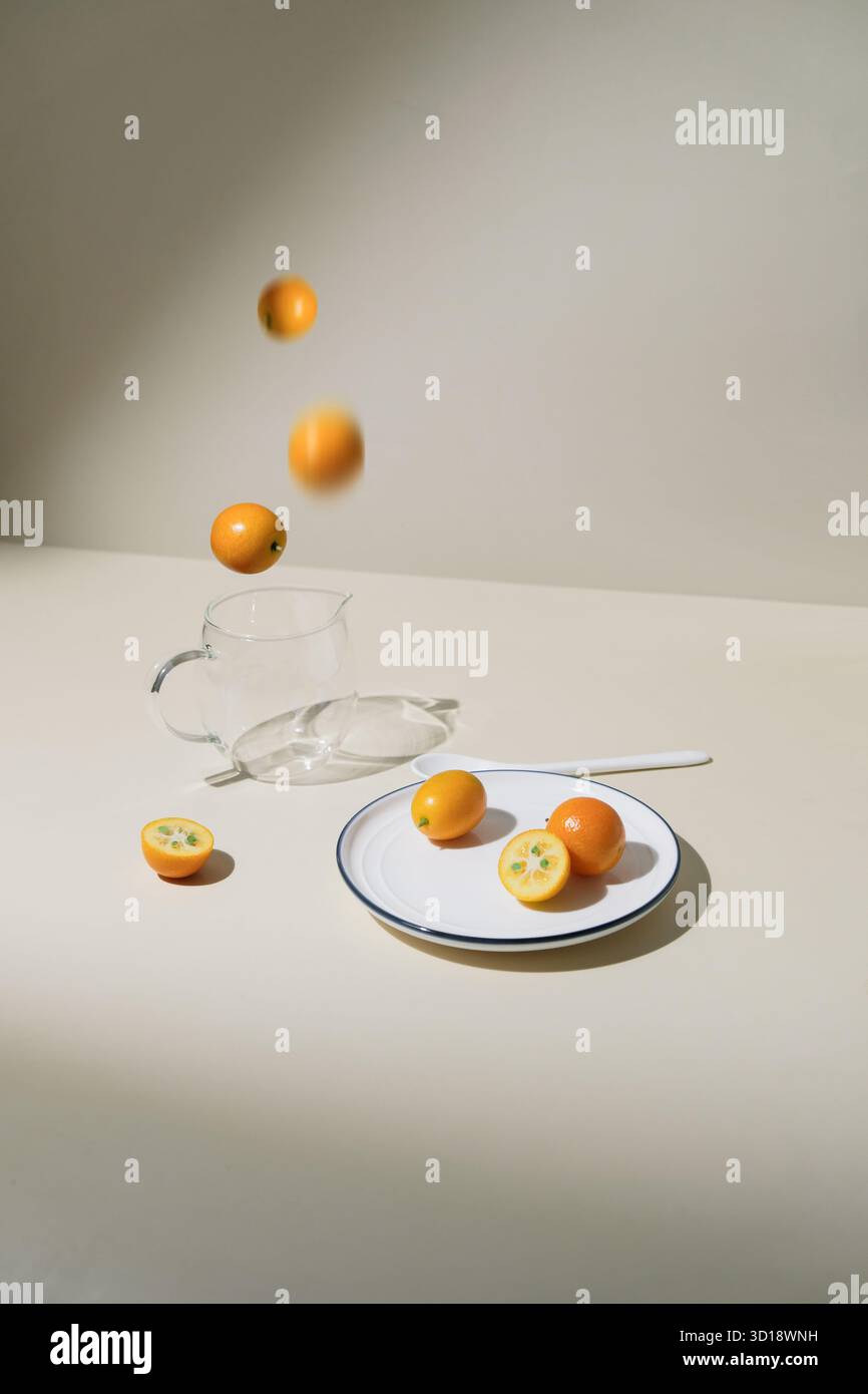 Kumquats tombant dans une tasse en verre. Kumquats frais tombant dans une tasse en verre sur une table beige, concept alimentaire minimal avec des agrumes et dos moderne propre Banque D'Images