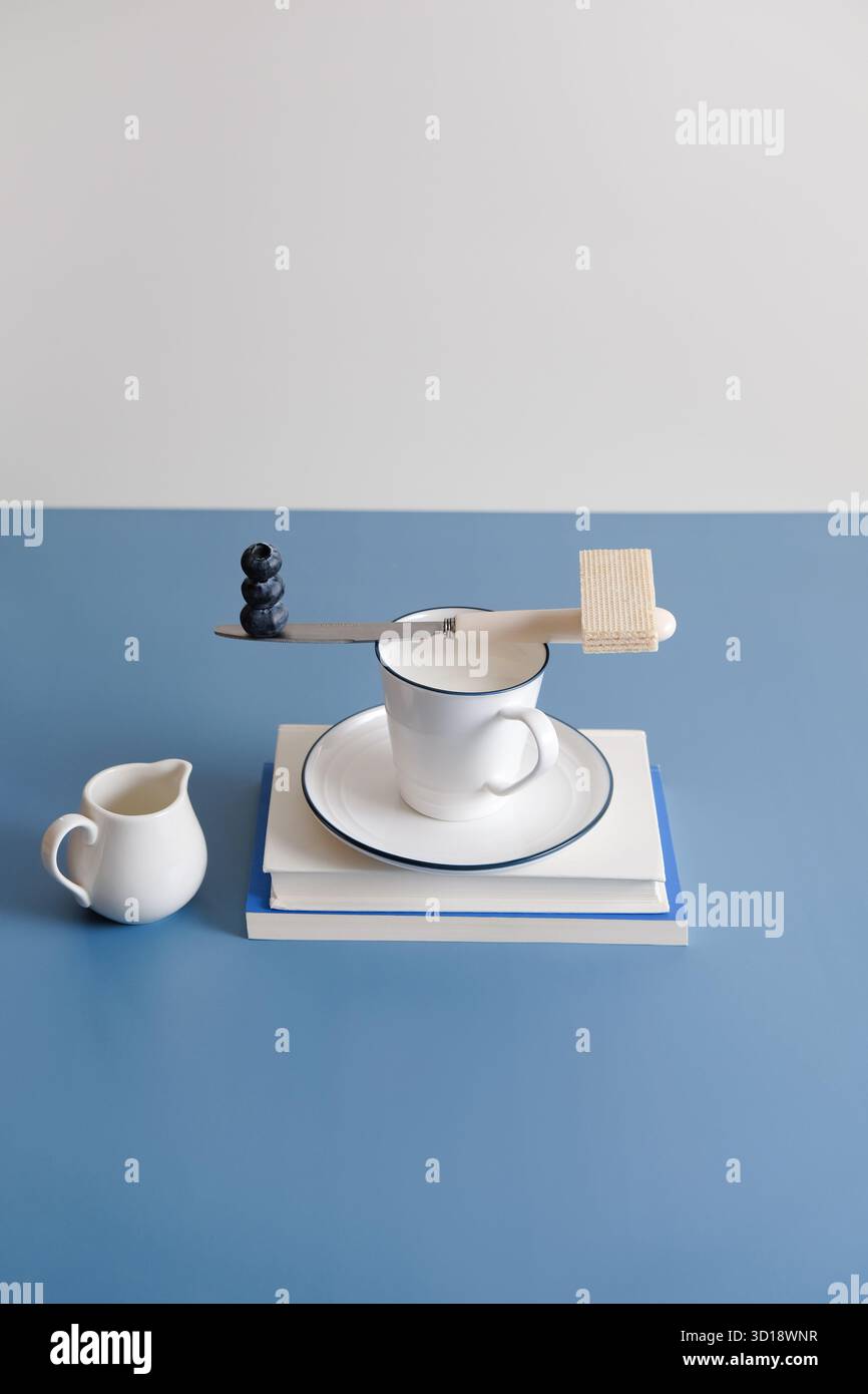 Bleuets et gaufrette sur tasse de lait. Équilibrer les bleuets et la gaufrette sur la tasse de lait avec fond de table bleu, concept alimentaire surréaliste minimal Banque D'Images