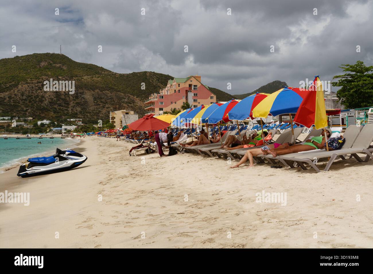 St Maarten - les amateurs de plage apprécient le soleil avec des fauteuils inclinables et des parasols colorés. Banque D'Images