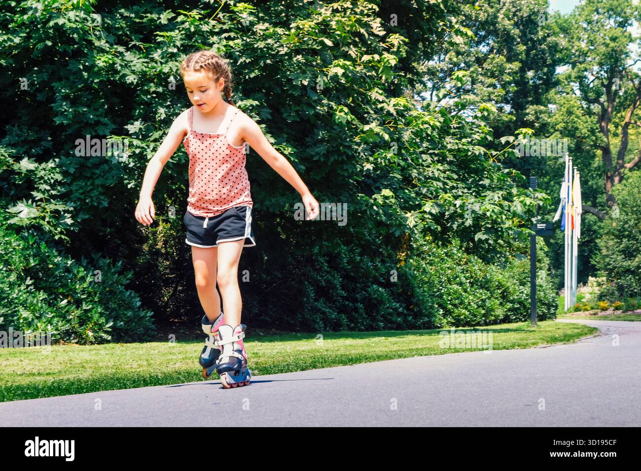 Fille sur patins à roulettes. Fille de 8-10 ans apprenant à patiner dans un parc d'été Banque D'Images