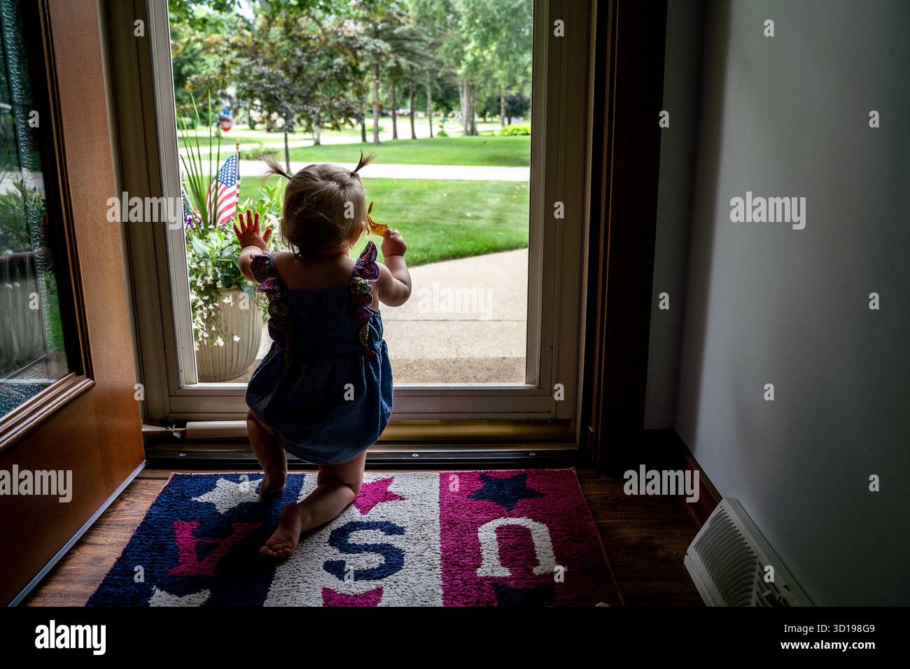 Bébé fille avec Pigtails regardant par la fenêtre de la porte d'entrée en été Banque D'Images