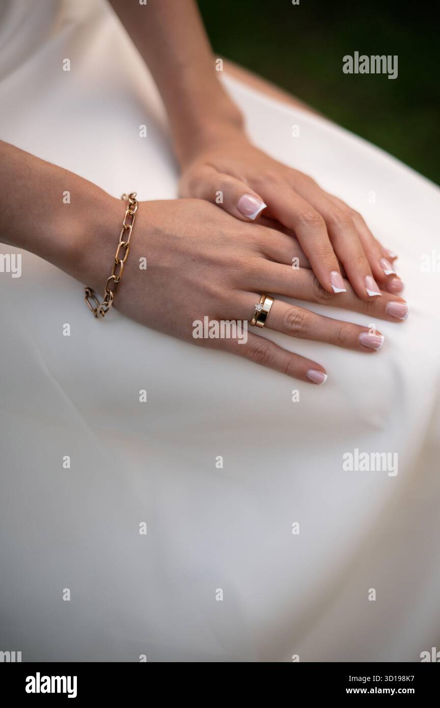 Mains élégantes avec bijoux en or sur robe blanche Banque D'Images