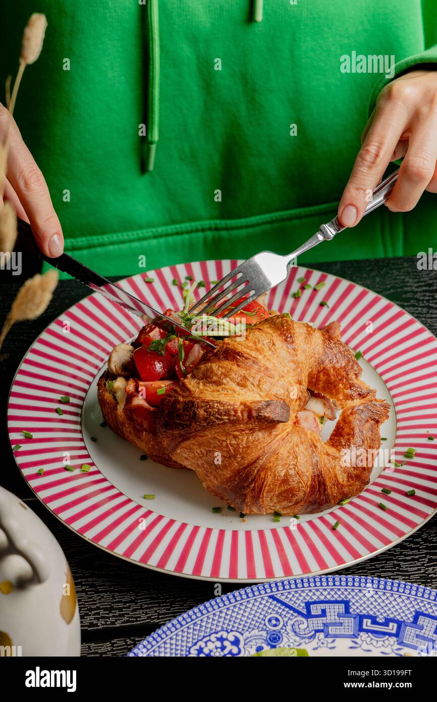Fille coupant un croissant avec un couteau et une fourchette Banque D'Images