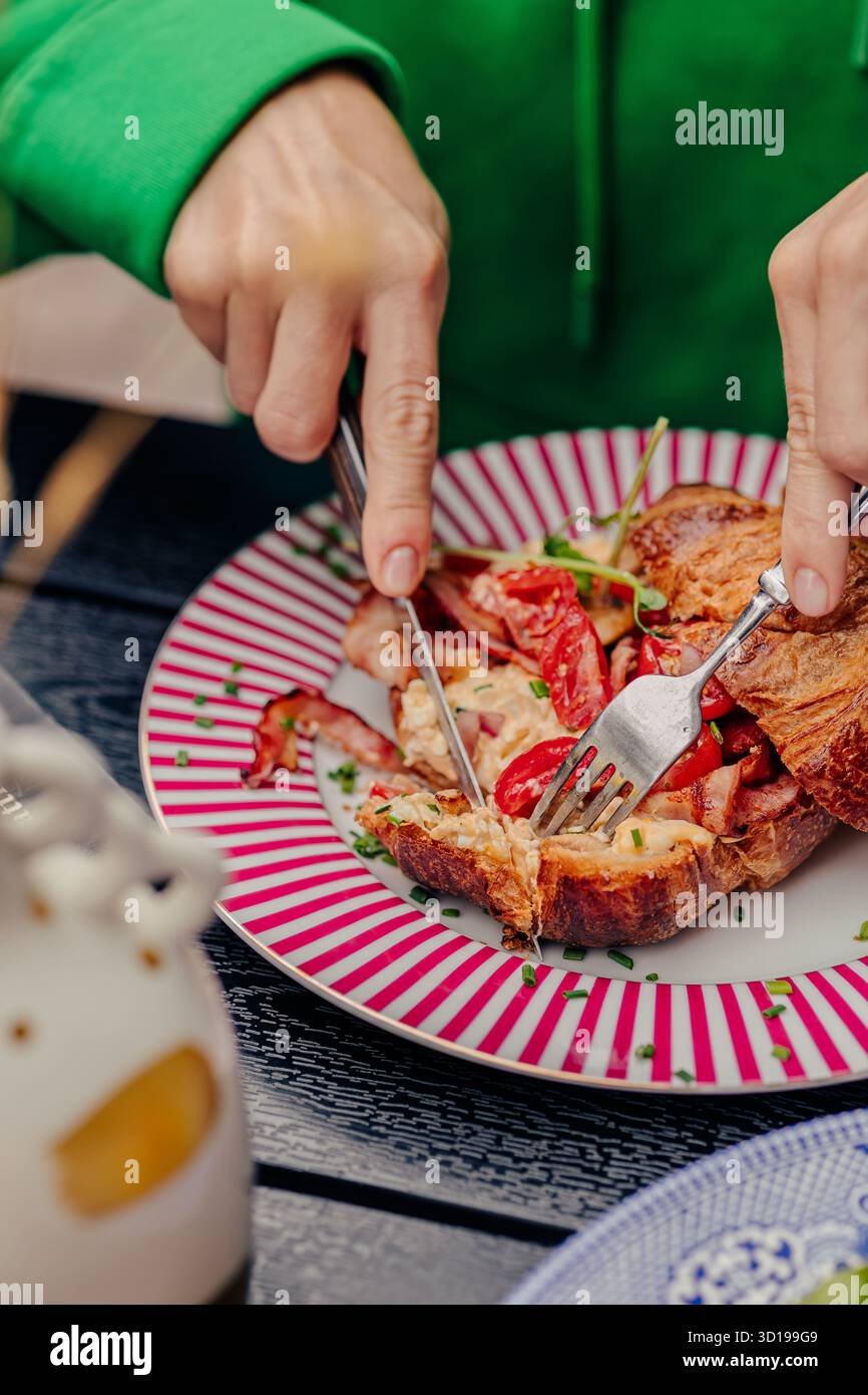 Fille coupant un croissant avec un couteau et une fourchette Banque D'Images