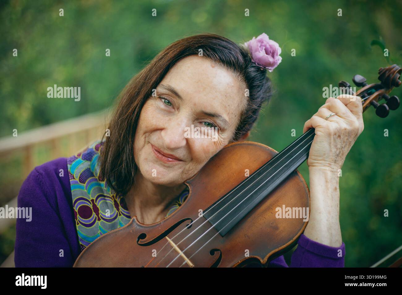 Une femme avec une fleur dans les cheveux tient un violon près de son visage Banque D'Images