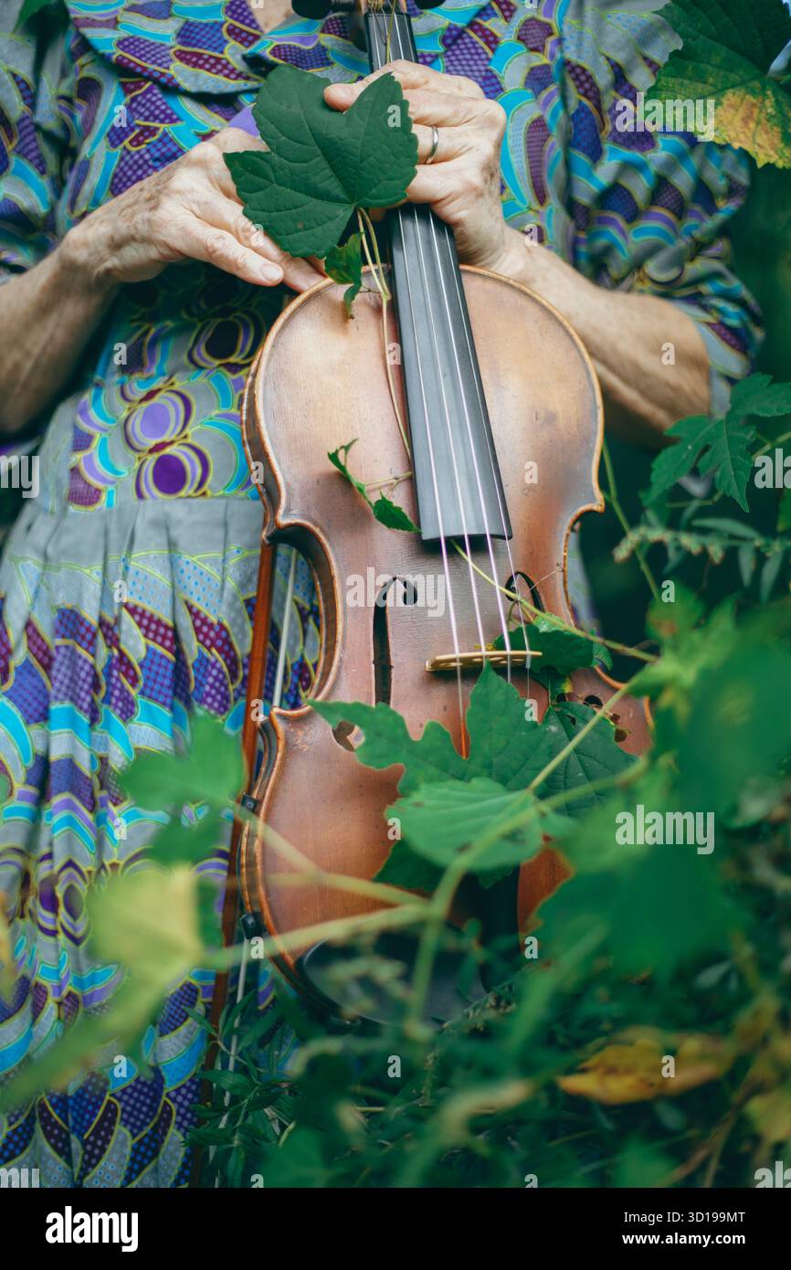 Une personne tient un violon parmi les feuilles vertes luxuriantes Banque D'Images