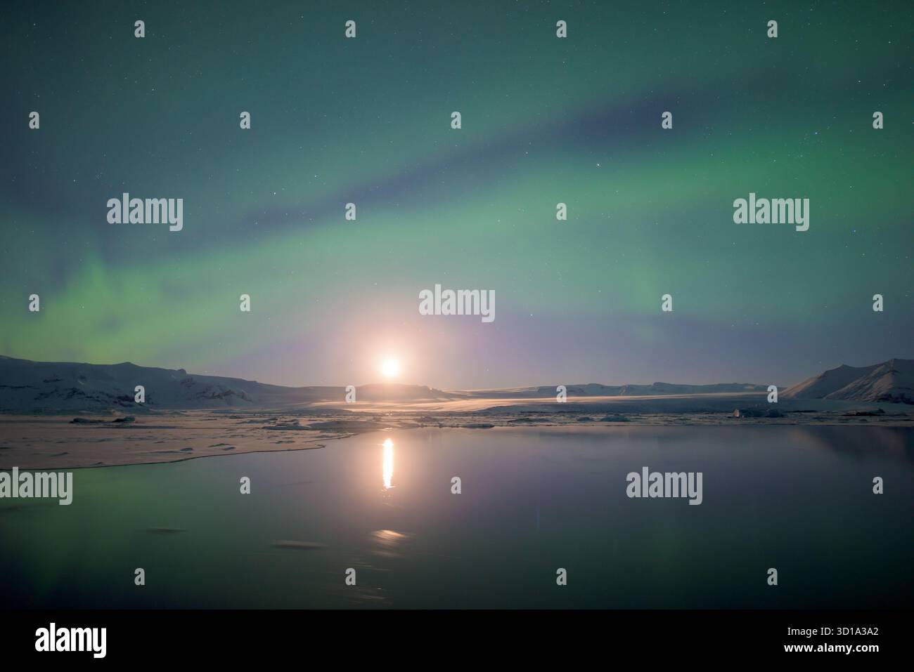 Vue sur les aurores boréales éthérées dansant au-dessus du lagon glacé, ses vrilles vertes reflétant le clair de lune sur l'eau plate, Jokulsarlon, Sveitarfélagið Hornafjörður, Islande. Banque D'Images