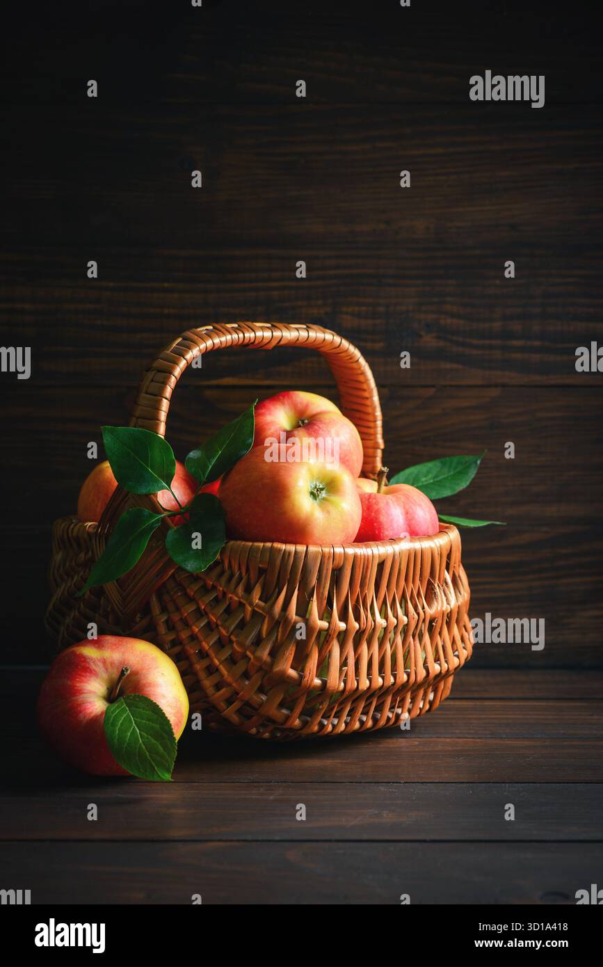 Pommes mûres dans un panier en osier sur un fond en bois Banque D'Images
