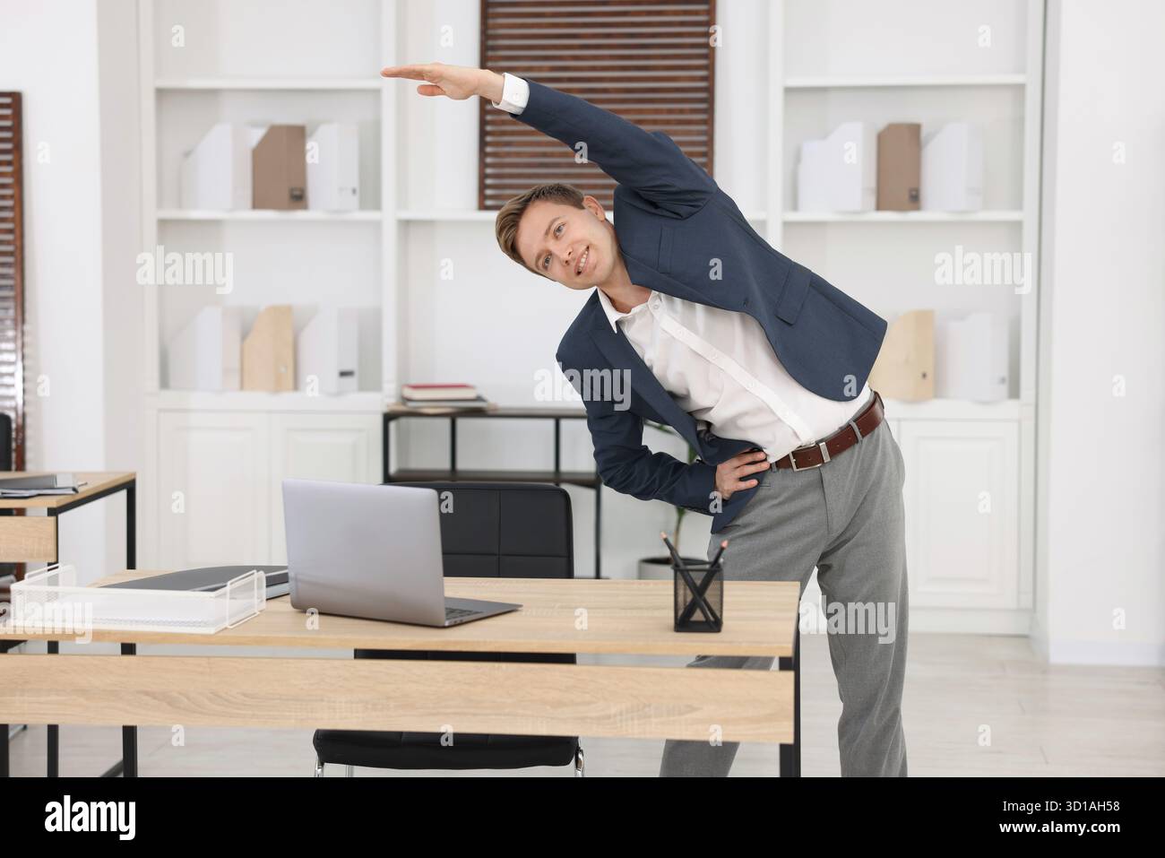 Jeune homme d'affaires faisant l'exercice d'étirement dans le bureau Banque D'Images