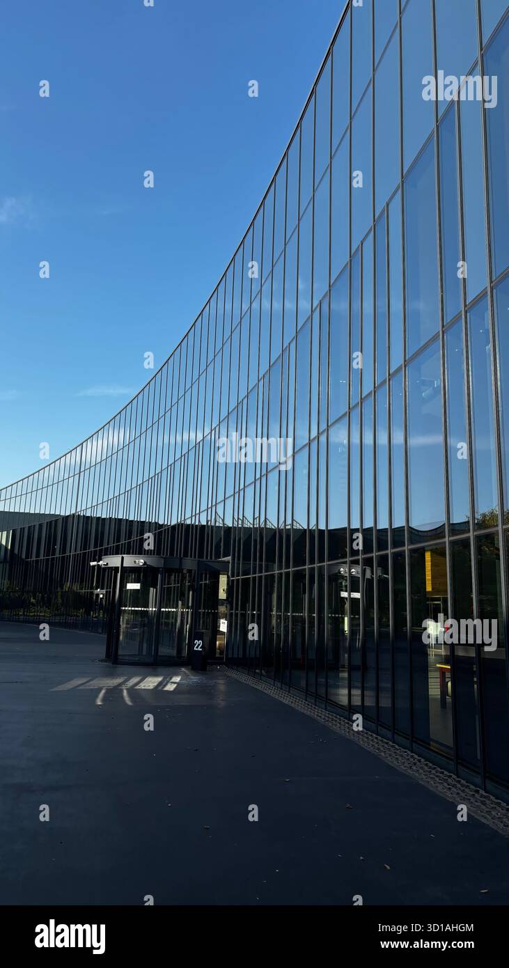 Façade en verre incurvée d'un bureau moderne ou d'un bâtiment commercial reflétant le ciel bleu clair et l'environnement environnant. - Image de stock capturée avec un smartphone