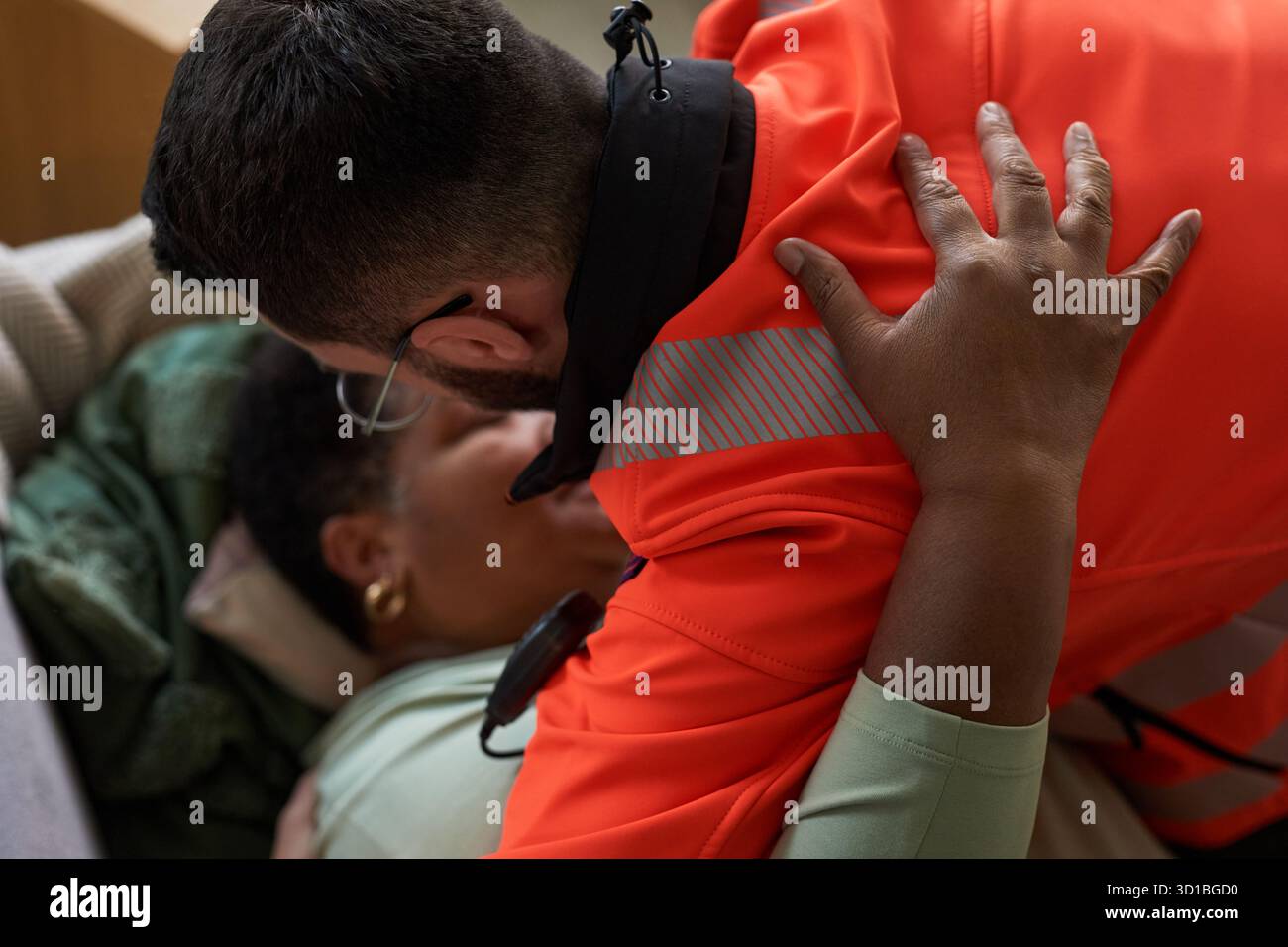 Femme noire d'âge moyen allongée sur le canapé aidée par un jeune adulte homme caucasien ambulant en uniforme, ambulant penché sur la fourniture de soins médicaux d'urgence Banque D'Images
