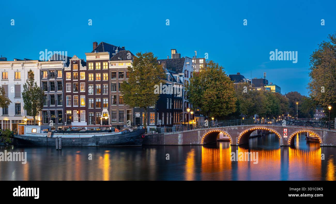 Crépuscule à Amsterdam, pont illuminé et maisons historiques reflétés dans la rivière Amstel Banque D'Images