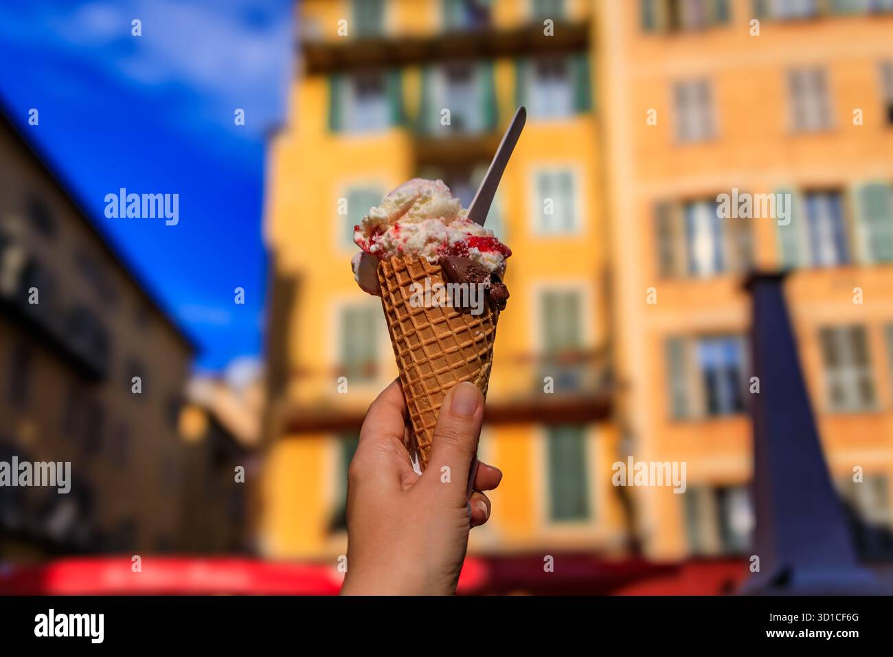 Main tient un cône de chocolat artisanal et amarena cerise gelato, vue sur les maisons colorées traditionnelles, vieille ville vieille ville, Nice, Sud de la France Banque D'Images