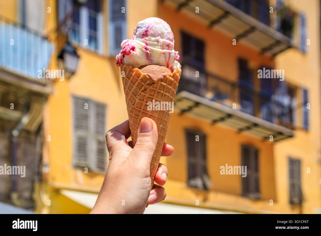 Main tient un cône de chocolat artisanal et amarena cerise gelato, vue sur les maisons colorées traditionnelles, vieille ville vieille ville, Nice, Sud de la France Banque D'Images