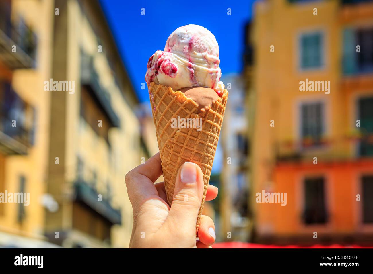 Main tient un cône de chocolat artisanal et amarena cerise gelato, vue sur les maisons colorées traditionnelles, vieille ville vieille ville, Nice, Sud de la France Banque D'Images
