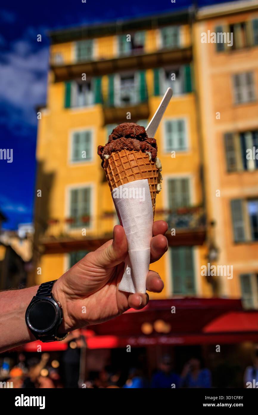 La main de l homme tient un cône de chocolat artisanal pistache gelato, vue sur les maisons colorées traditionnelles, vieille ville de Nice, Sud de la France Banque D'Images