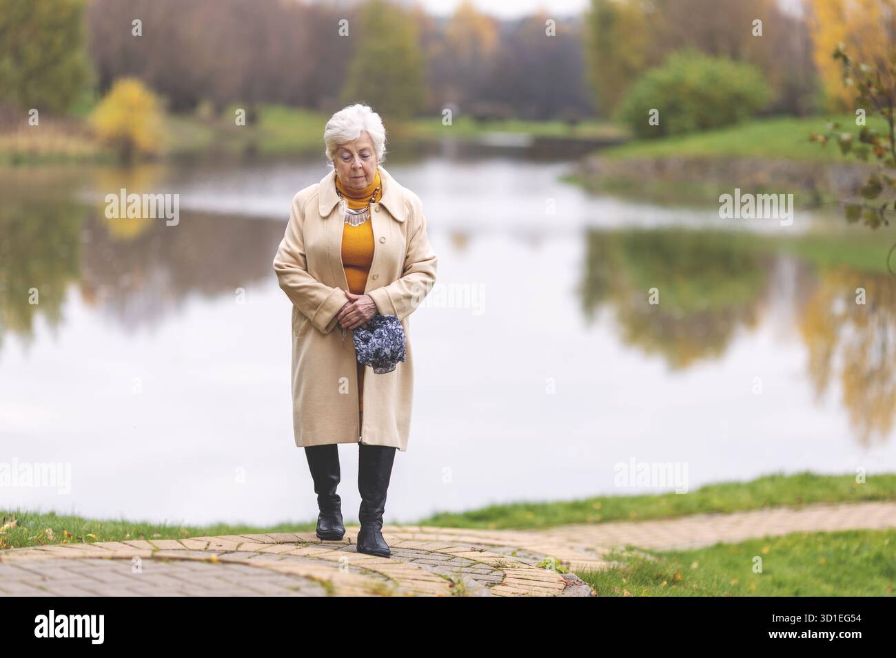 Femme caucasienne âgée marchant dans le parc d'automne seul. Dame senior appréciant la promenade paisible au bord du lac. Détente de la saison d'automne Banque D'Images