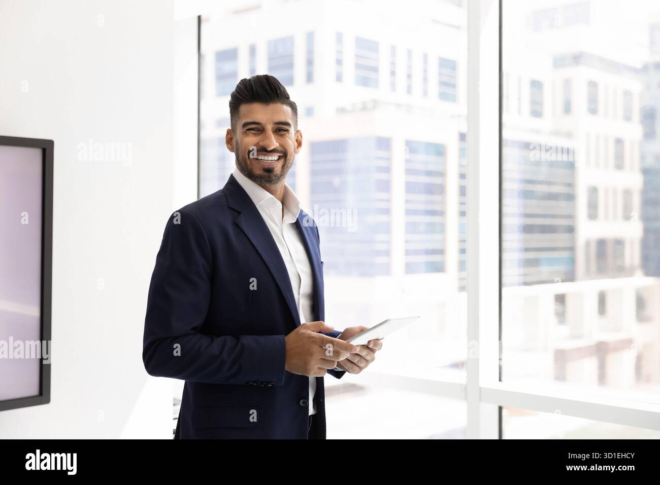 Joyeux jeune homme d'affaires indien dans élégant costume formel tenant la tablette Banque D'Images