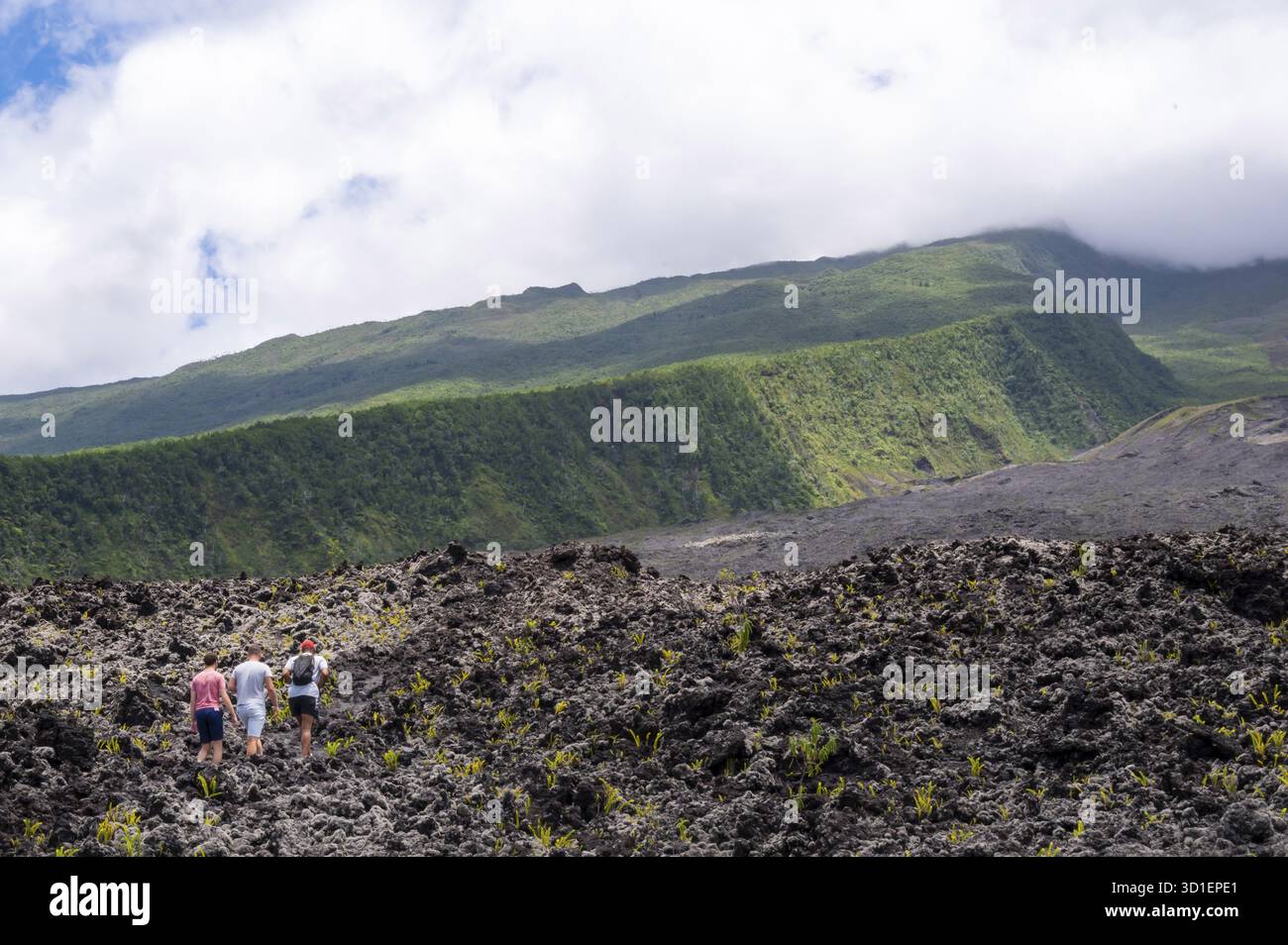 Trois randonneurs en tenue décontractée traversent une vaste plaine de lave accidentée de la Grand Brule avec une végétation naissante et des roches de lave noires devant le Banque D'Images