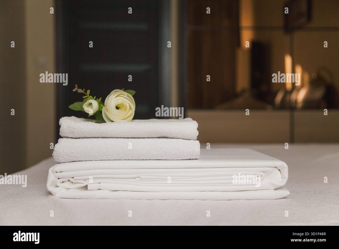 Trois serviettes douces et blanches sont soigneusement empilées sur une table de spa. Une seule fleur ajoute une touche d'élégance. Le cadre est serein, parfait pour la détente et Banque D'Images