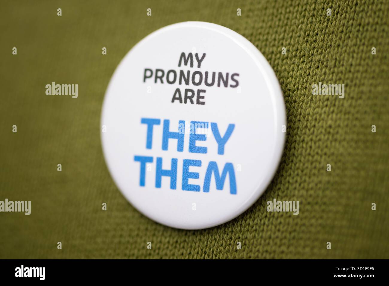 Un badge portant les mots « My pronoms are They » est porté sur un pull vert olive Banque D'Images