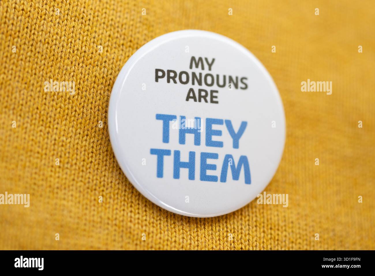 Un badge portant les mots « My pronoms are They » est porté sur un pull jaune. Banque D'Images