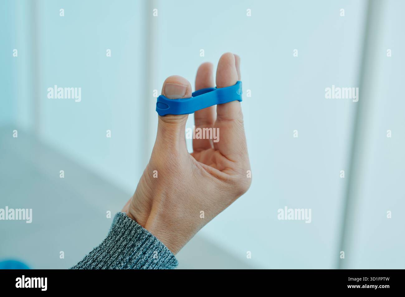 un homme exerçant sa main avec une bande élastique bleue, étirant ses doigts pour renforcer ses muscles et améliorer sa mobilité pendant une séance de rééducation Banque D'Images