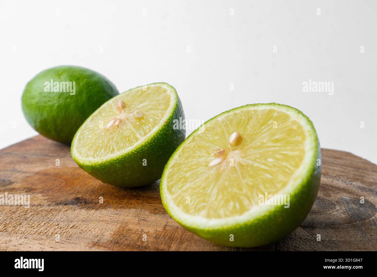 Gros plan de citrons verts frais, entiers et tranchés. Les agrumes sont sur une planche à découper en bois rustique avec un fond blanc propre. Banque D'Images