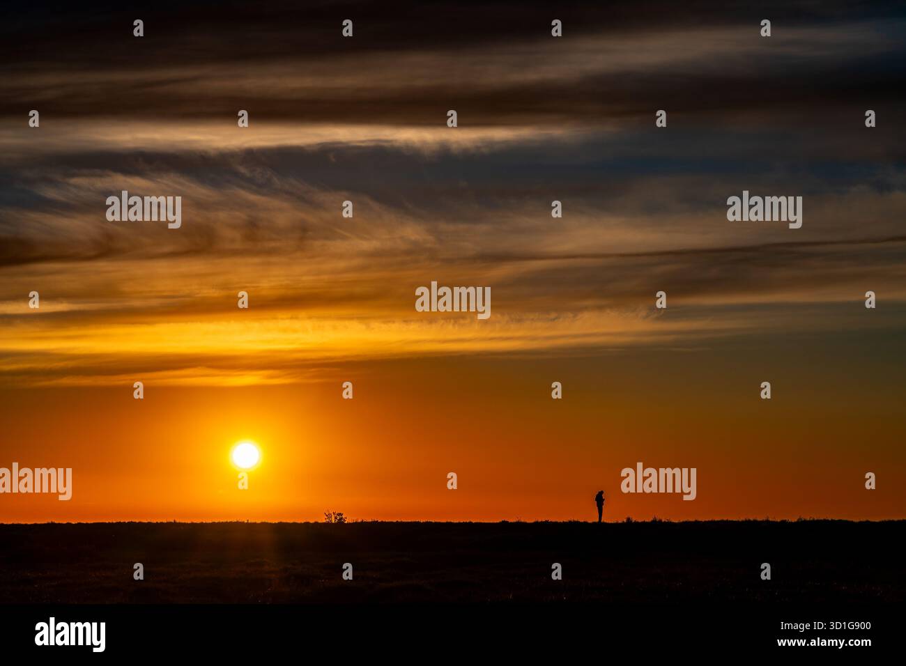 Silhouette d'une personne regardant le lever du soleil sous le ciel incandescent Banque D'Images