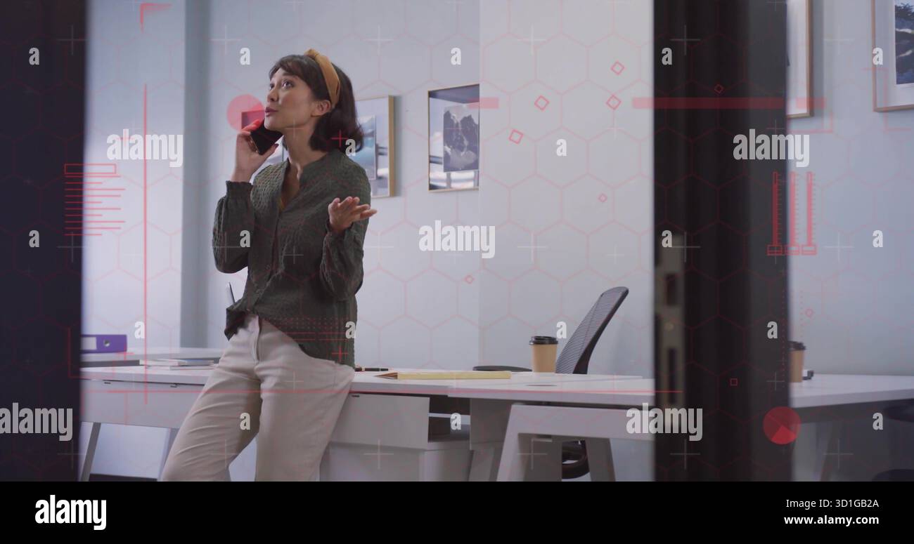 Femme asiatique penchée tenant smartphone et faisant des gestes au bureau avec ordinateur portable, papiers et café Banque D'Images