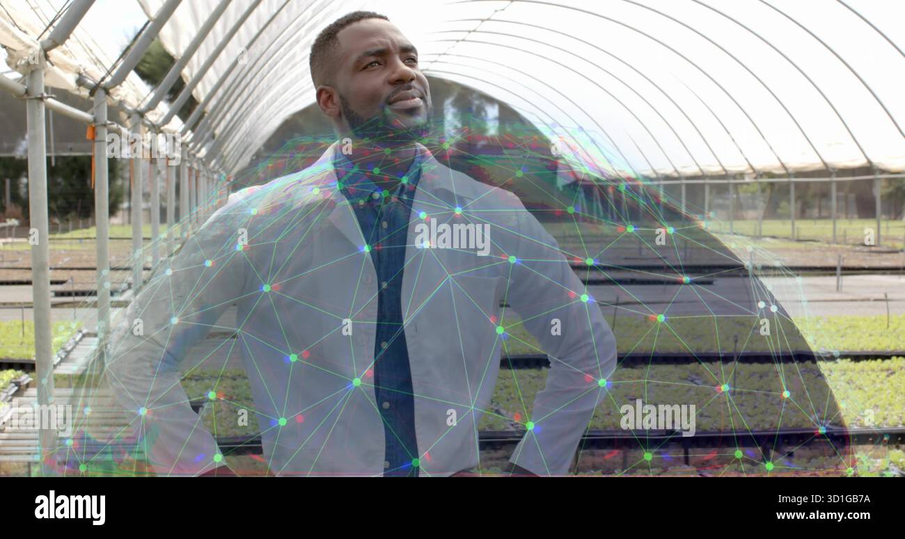 Chercheur debout en blouse de laboratoire arpentant des bancs en métal de serre avec des plateaux de semis Banque D'Images