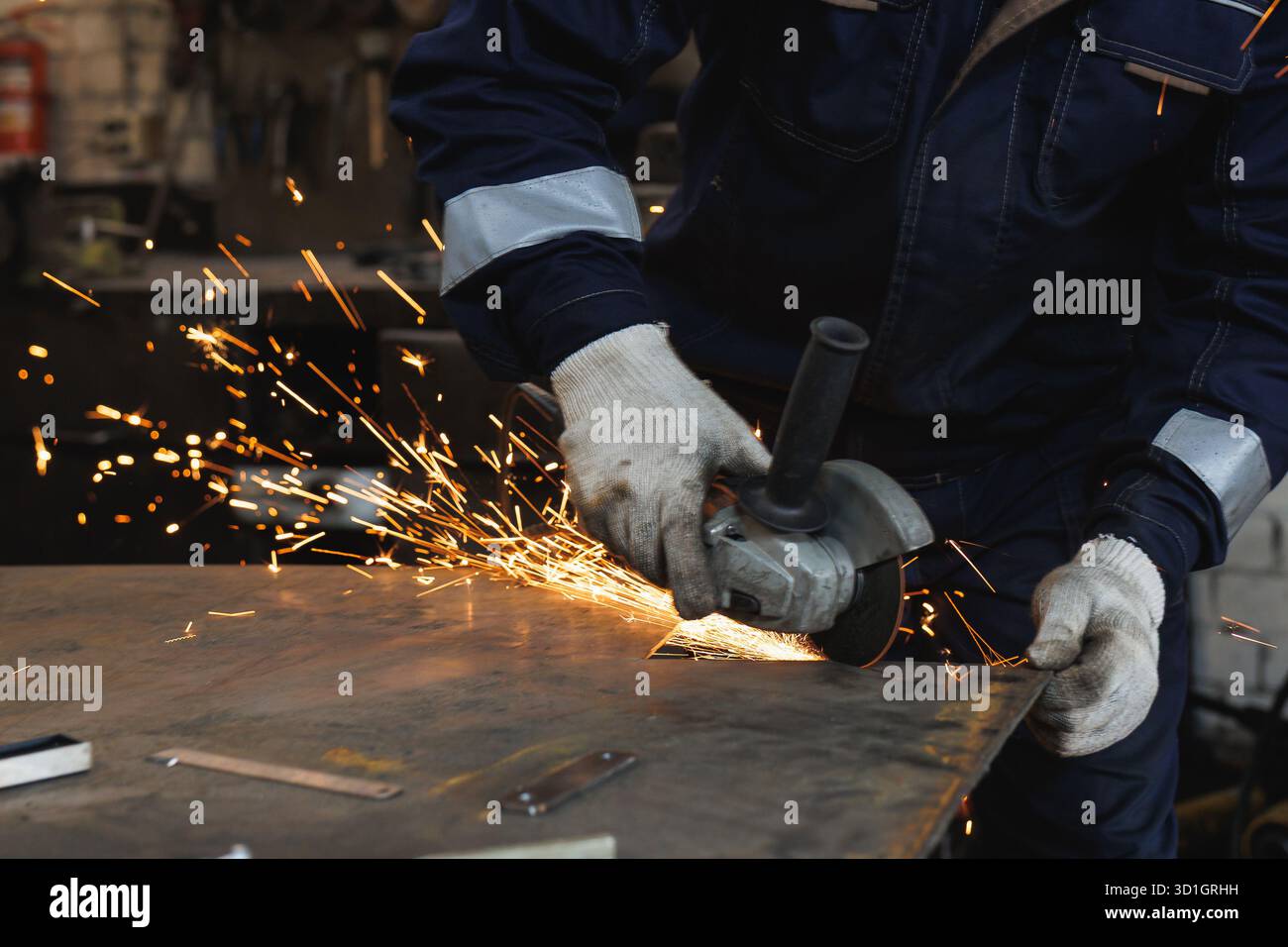 Un homme meule diligemment un morceau de métal à l'aide d'un broyeur puissant, mettant en valeur l'art du travail des métaux dans un environnement bleu Banque D'Images