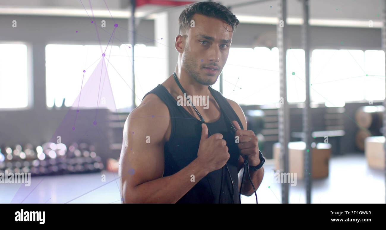 Amateur de fitness masculin debout saisissant la corde à sauter autour du cou dans une salle de gym spacieuse, avec porte-haltères Banque D'Images