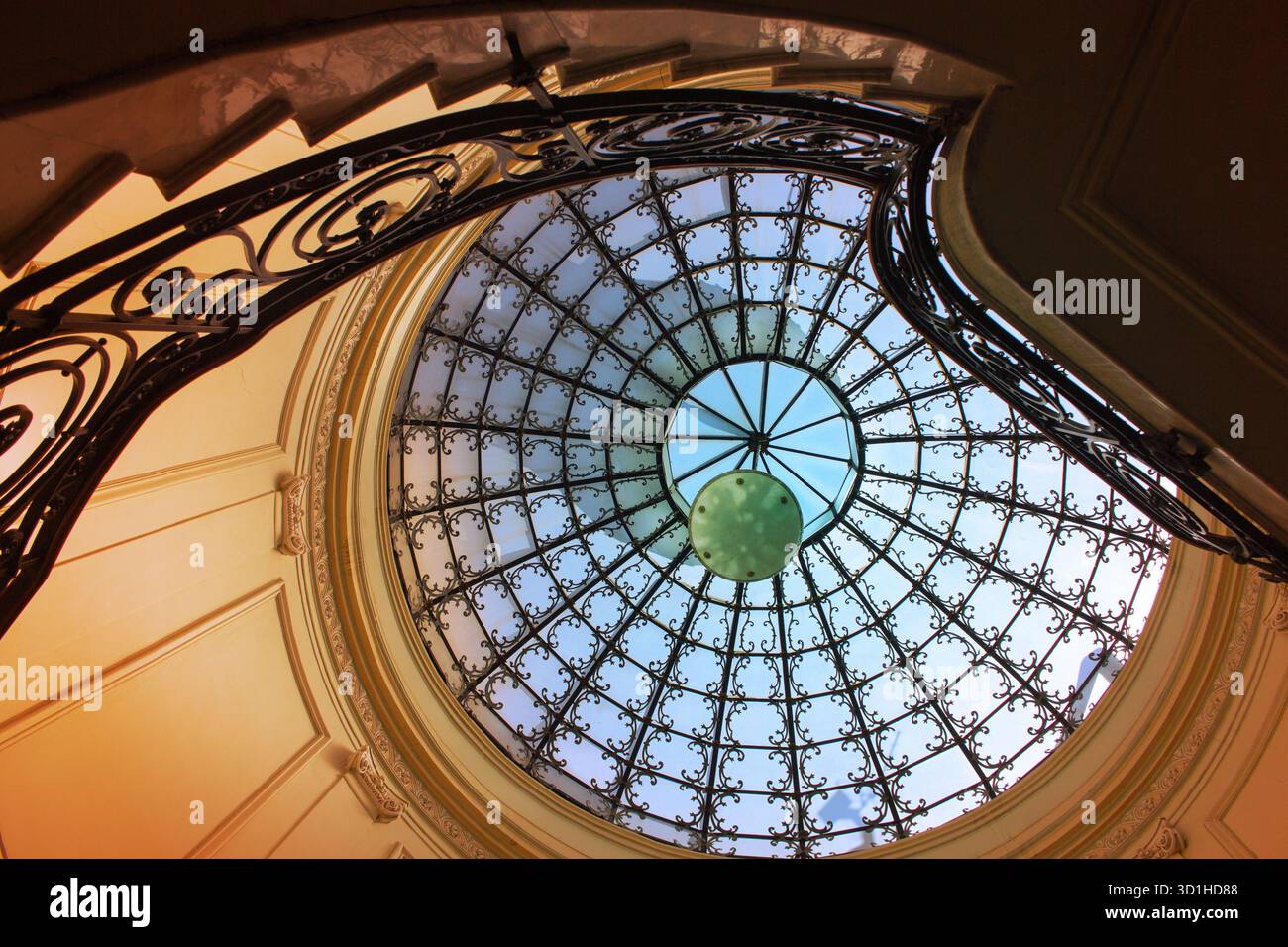 Élégant plafond dôme en fer et en verre avec escalier courbé et lumière chaude, détail architectural vintage avec symétrie artistique et design classique Banque D'Images