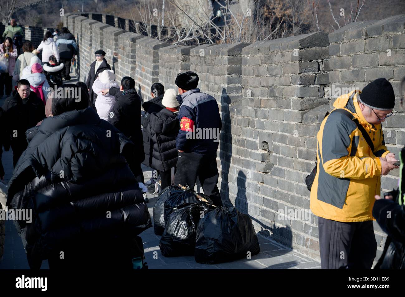 Au milieu du flux régulier de visiteurs, un agent de sanition se tient à côté de sacs poubelles noirs le long de la Grande Muraille Banque D'Images