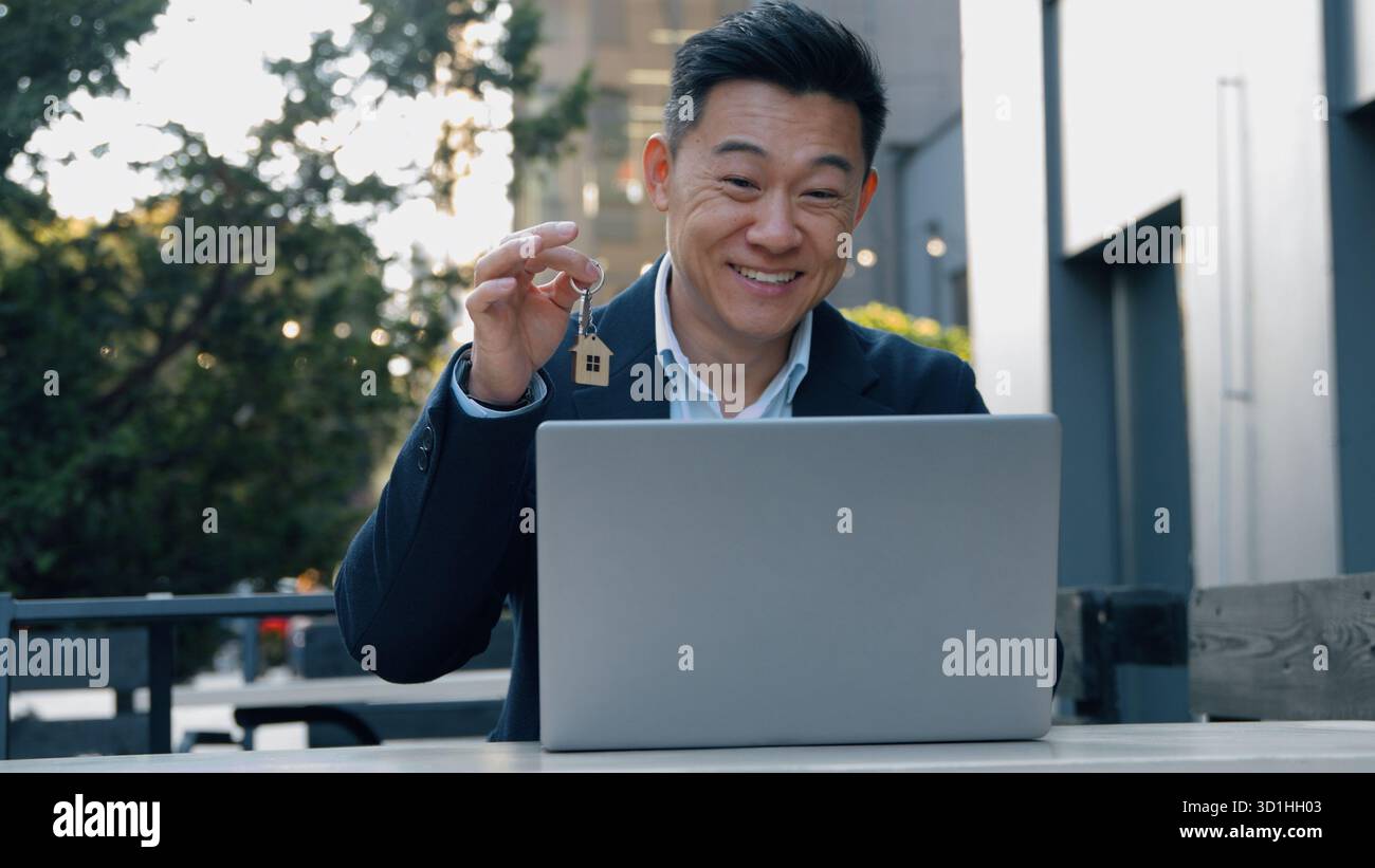 Heureux souriant homme d'affaires asiatique montrant la clé parler vidéo appeler homme d'affaires coréen dans la conférence de conversation de ville avec ordinateur portable se réjouir appartement propre maison Banque D'Images