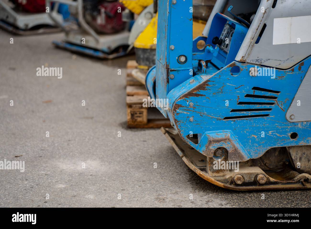 Vue rapprochée d'une machine de compacteur à plaque vibrante industrielle avec peinture bleue usée sur la surface d'asphalte présentant l'équipement de construction extra-robuste utilisé f Banque D'Images