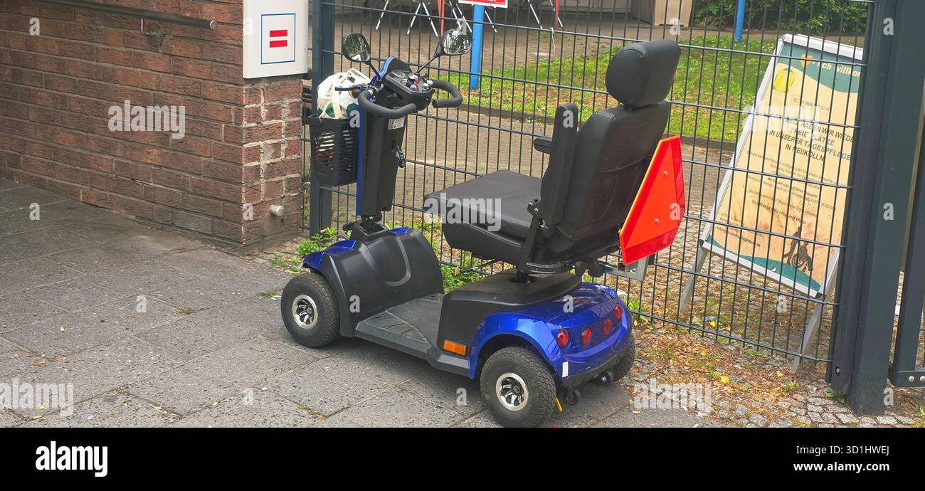 Belin, Allemagne - 19 mai 2025 : scooter de mobilité bleu est garé à côté d'une clôture dans un cadre urbain avec signalisation visible. Banque D'Images