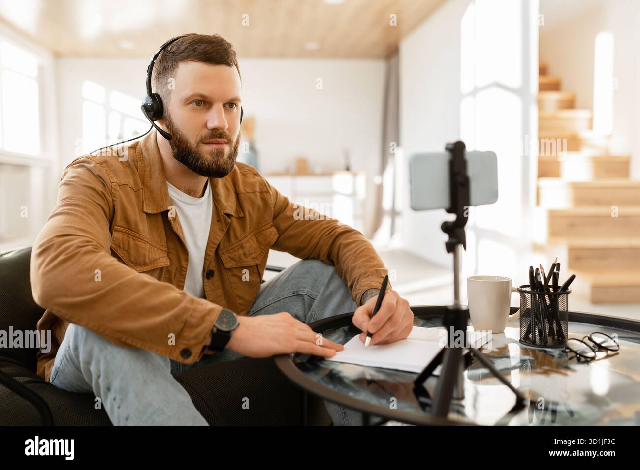 Homme étudiant à la maison avec des écouteurs et bloc-notes tout en assistant à un cours en ligne ou une réunion Banque D'Images