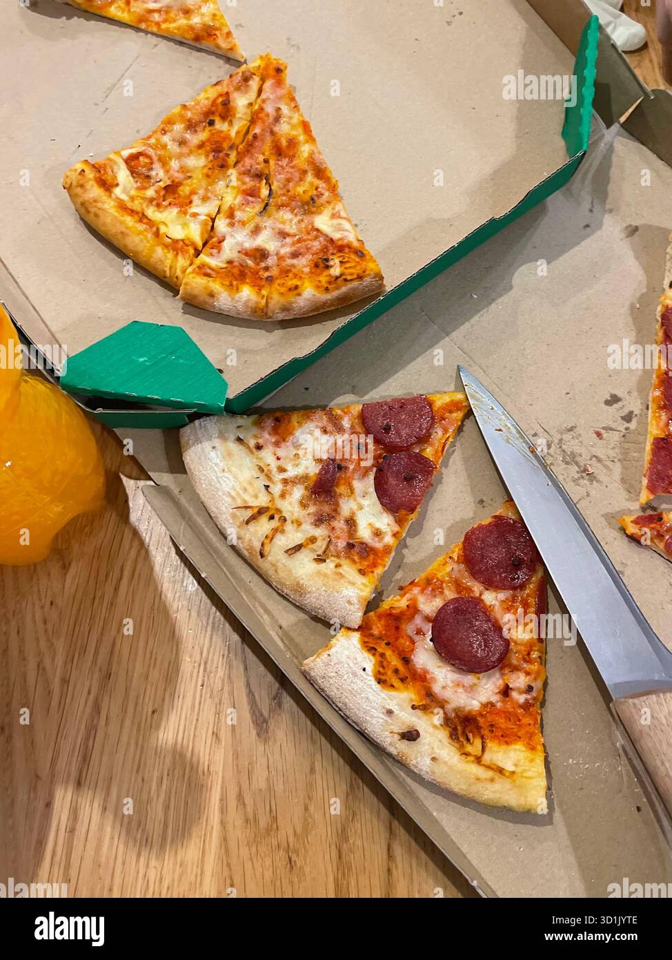Gros plan de tranches de pizza restantes dans une boîte de livraison en carton sur une table en bois. Tranches garnies de saucisse pepperoni et fromage. Un couteau couché à proximité Banque D'Images