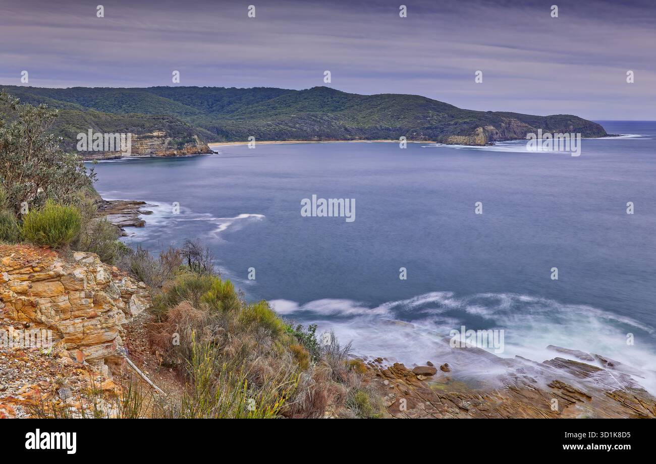Image longue exposition de l'océan calme dans une baie avec des promontoires boisés un jour couvert au parc national de Bouddi, Nouvelle-Galles du Sud, Australie Banque D'Images